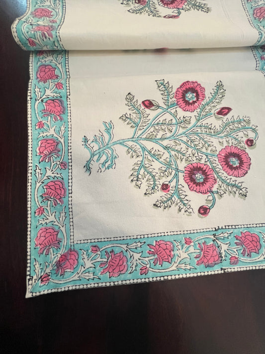 Close-up of floral table runner showcasing pink and turquoise embroidery on a white cotton base