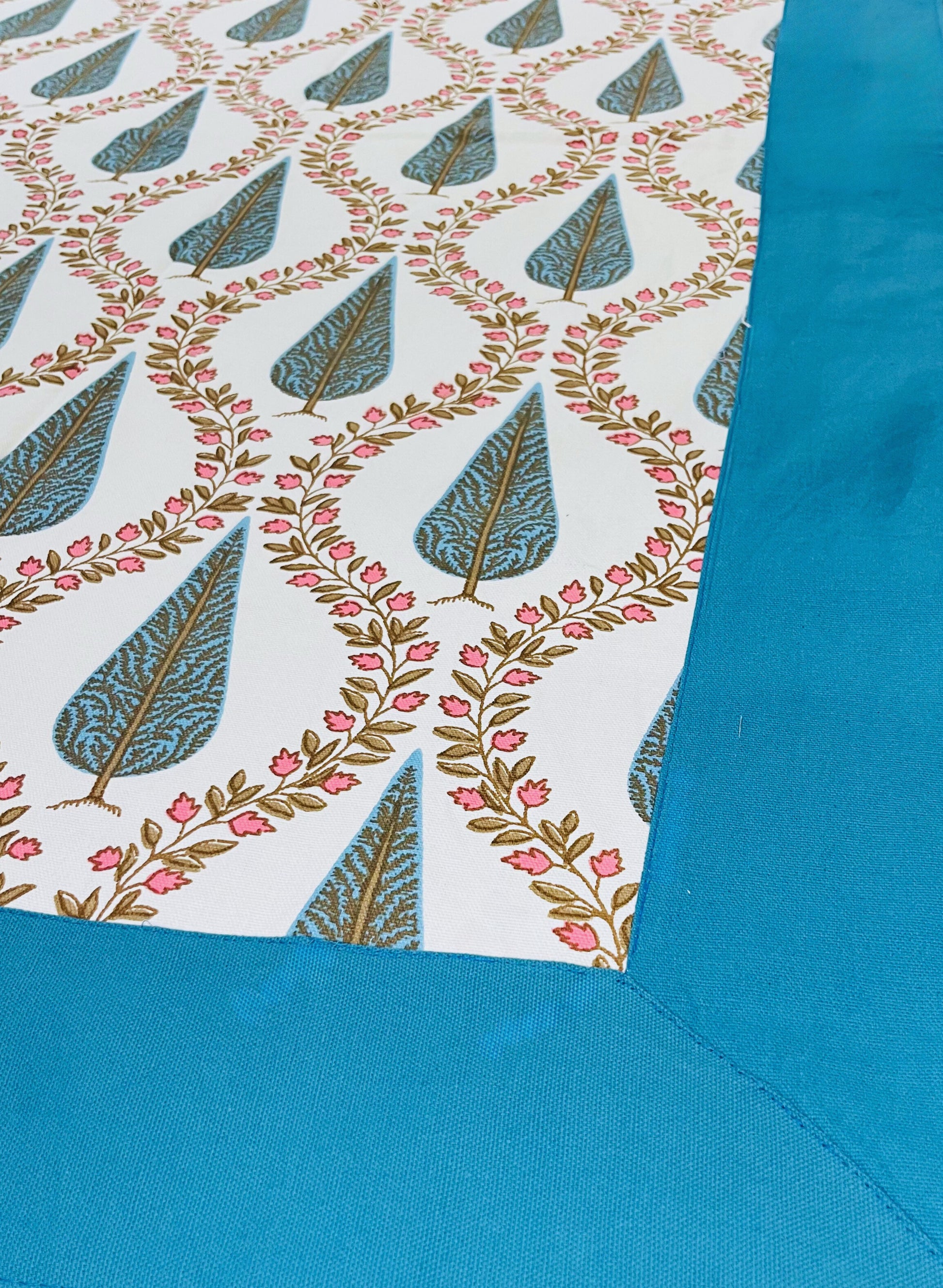Close-up of floral block print table cover featuring blue and white fabric with pink flowers and a traditional leaf pattern with a turquoise border
