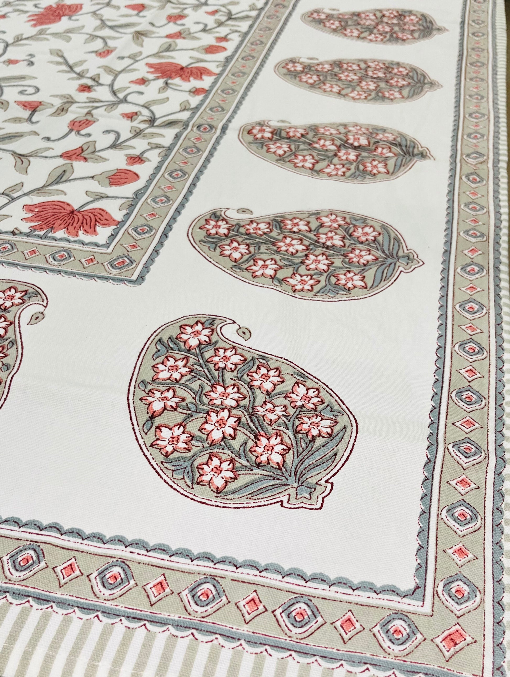 Close-up of floral block print cotton tablecloth featuring coral and grey motifs with a decorative border pattern