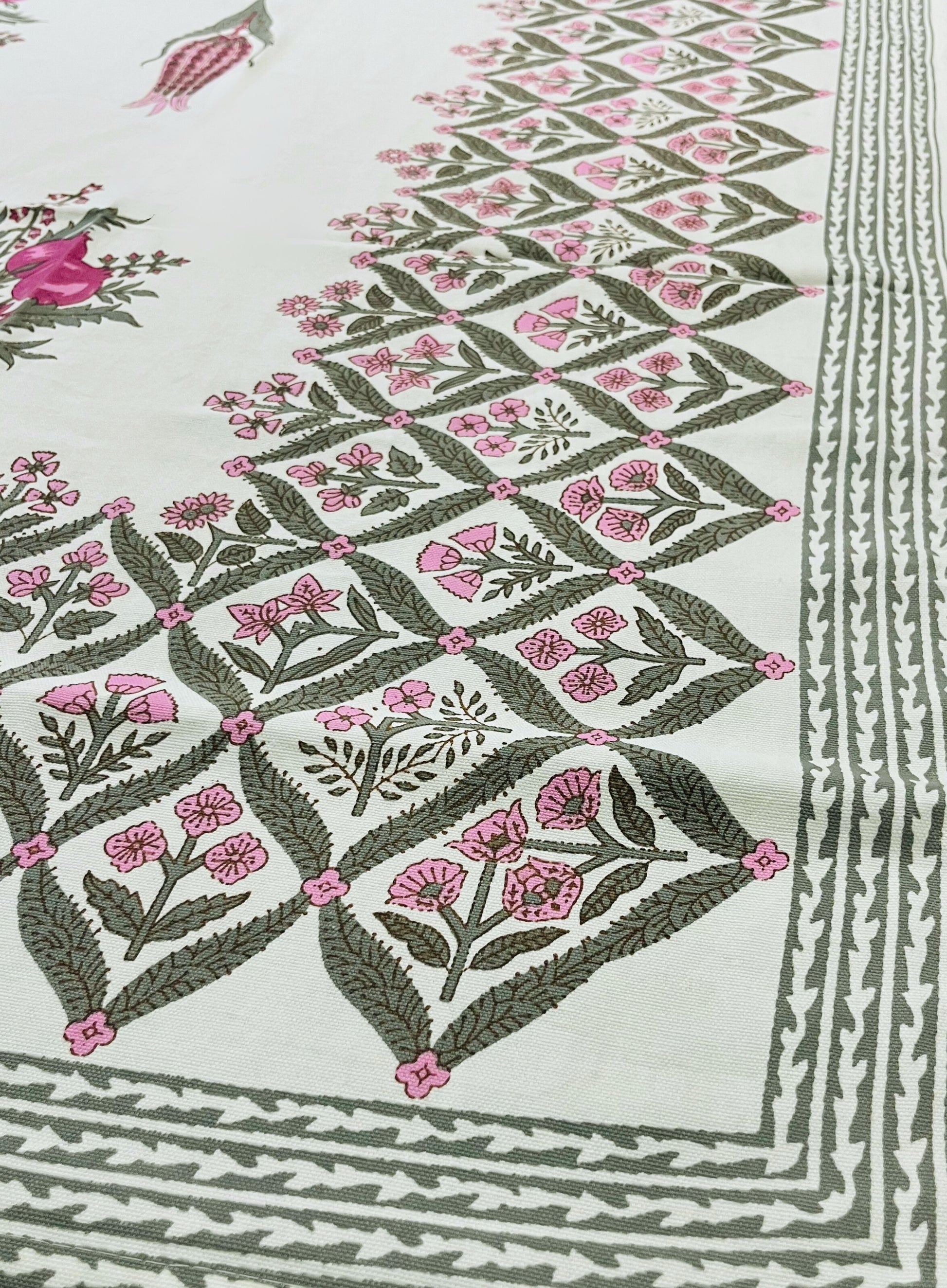 Close-up of floral block print tablecloth featuring a traditional pink and green design on a white cotton fabric