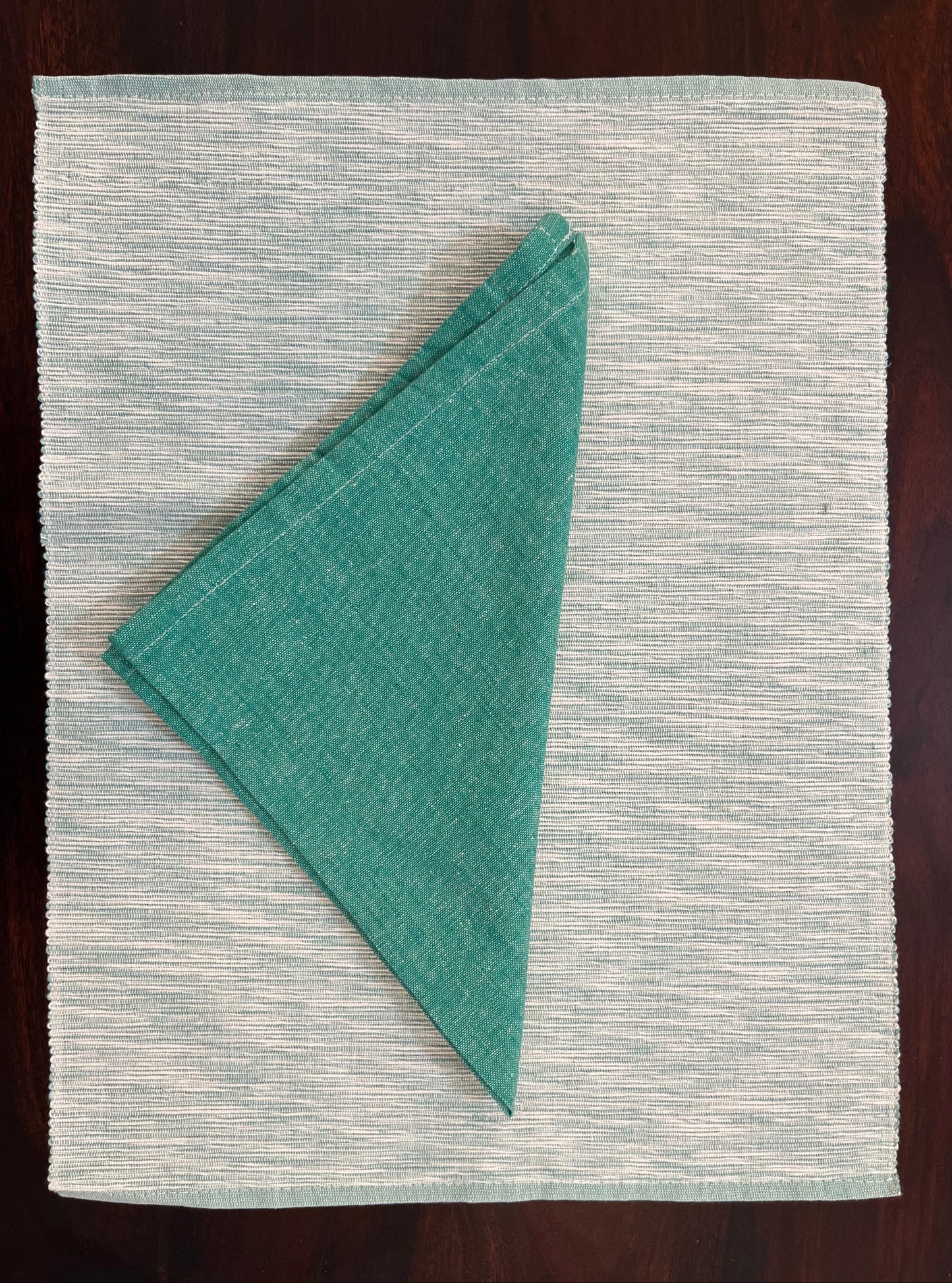 Close-up of placemats and napkins showcasing intricate teal green woven texture and fine fabric detailing