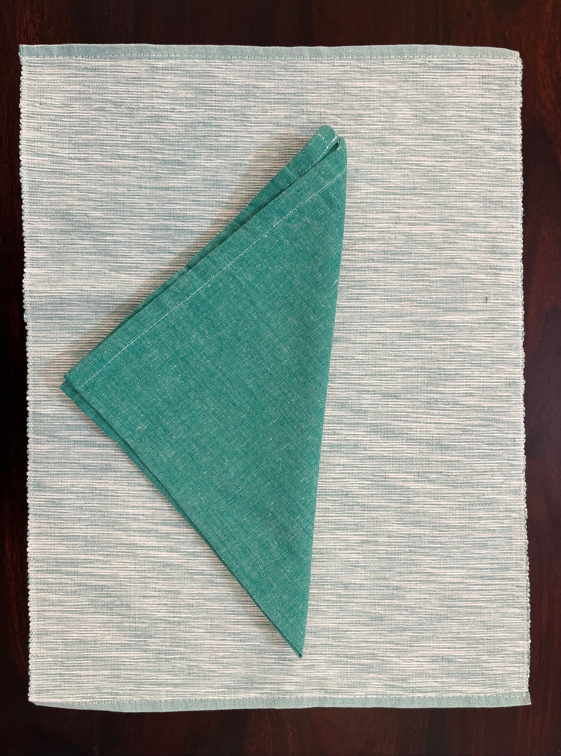 Close-up of placemats and napkins showcasing intricate teal green woven texture and fine fabric detailing
