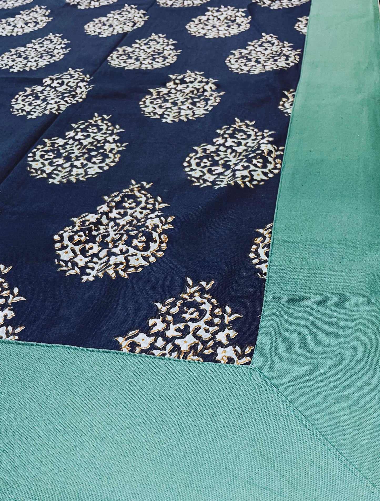 Close-up of decorative dining table cover featuring a navy blue floral paisley pattern with a green border