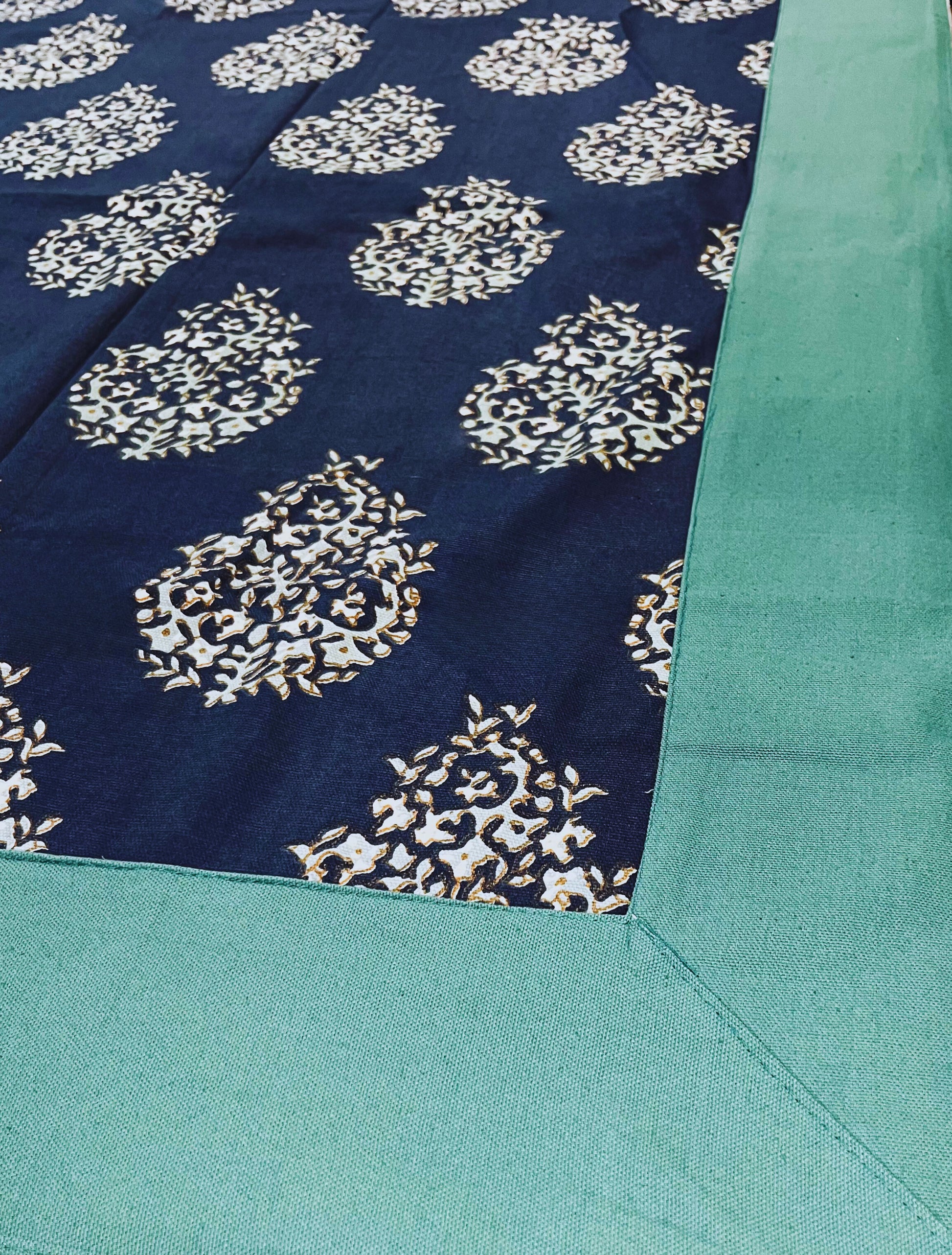 Close-up of decorative dining table cover featuring a navy blue floral paisley pattern with a green border