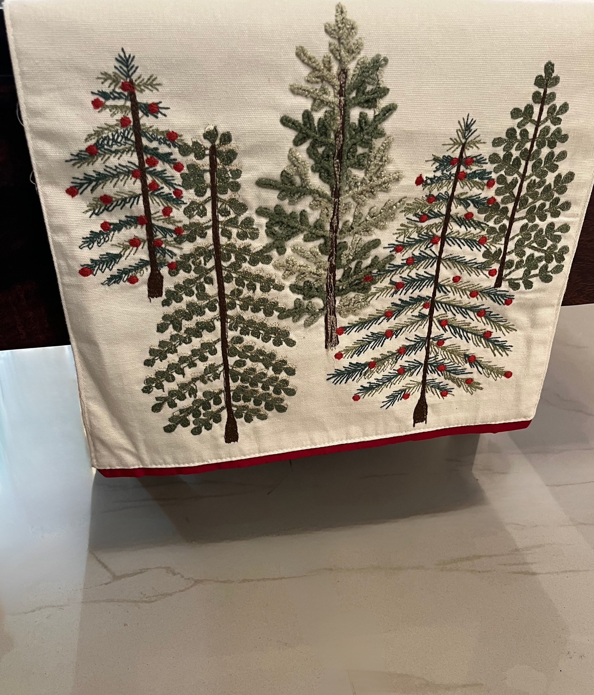 Embroidered table runner featuring a decorative pine pattern with red berries, cream background, and red trim