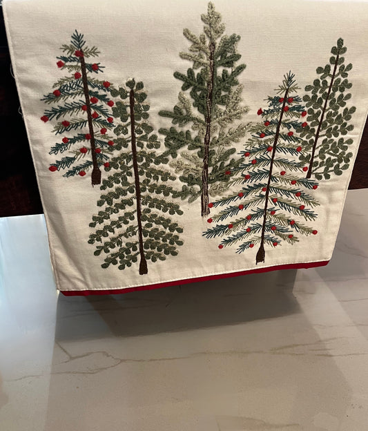 Embroidered table runner featuring a decorative pine pattern with red berries, cream background, and red trim