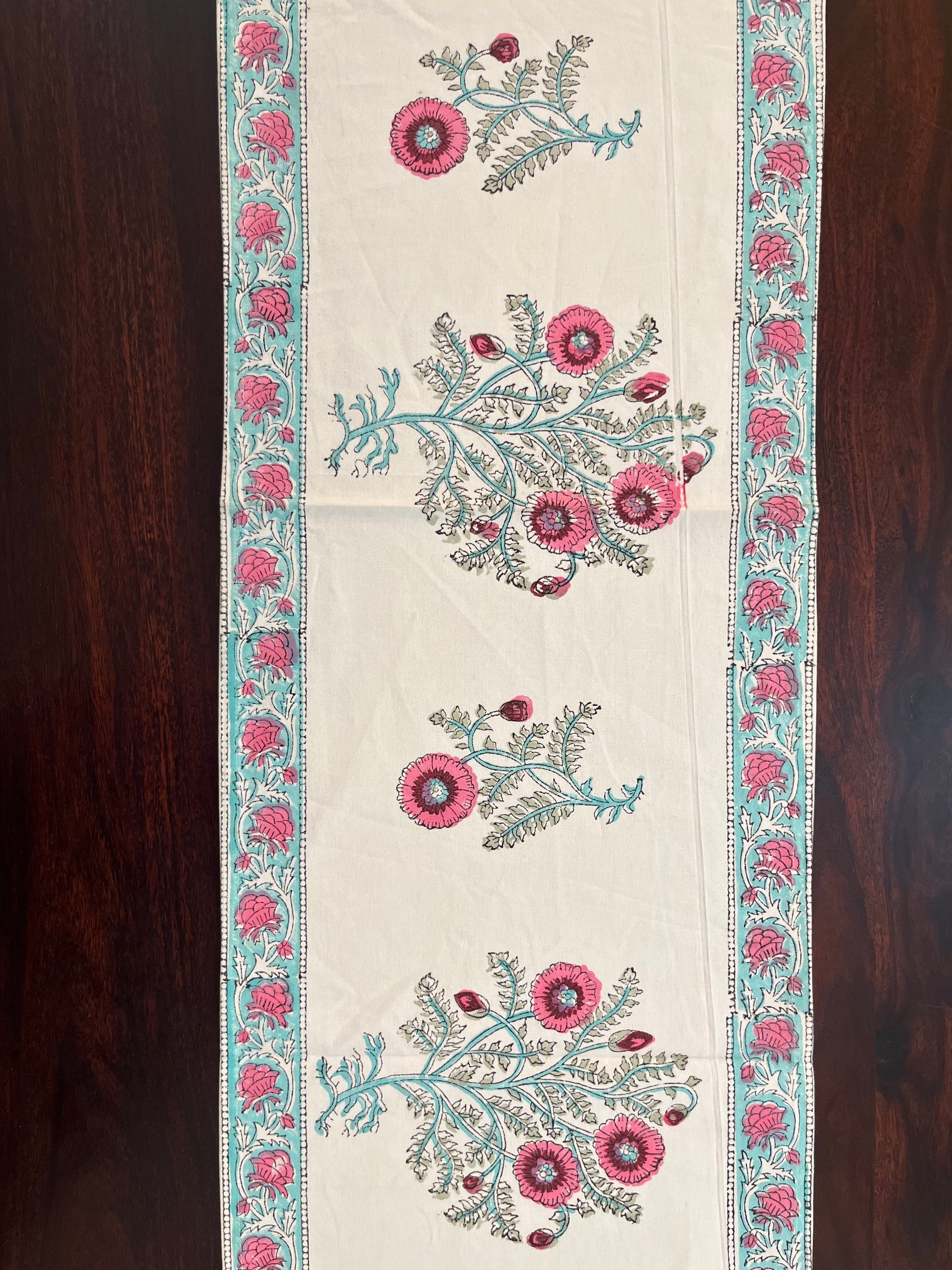 Floral table runner featuring a pink and turquoise embroidered design on a white cotton base