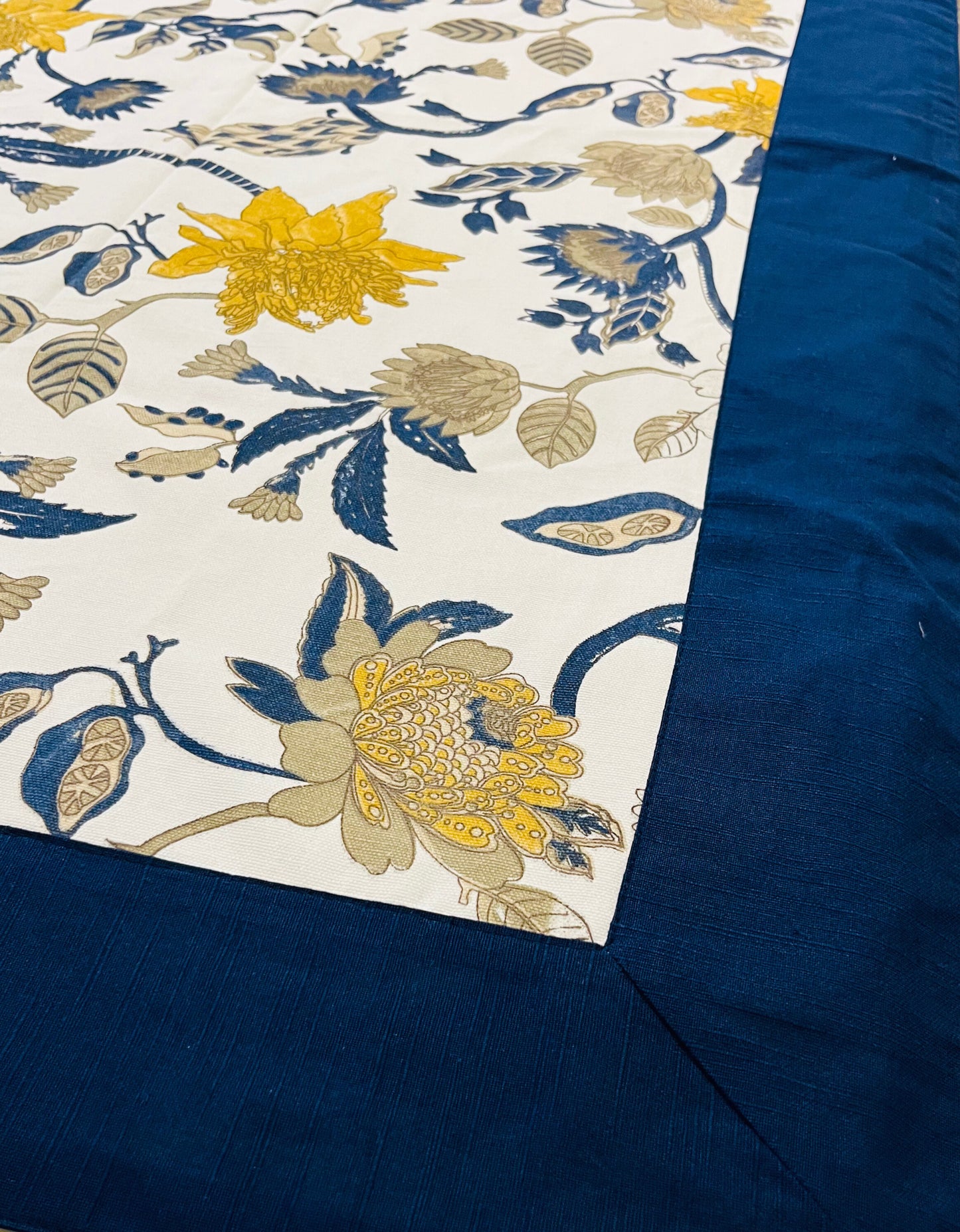 Close-up of floral tablecloth featuring yellow and blue flowers on a white background with a navy blue border