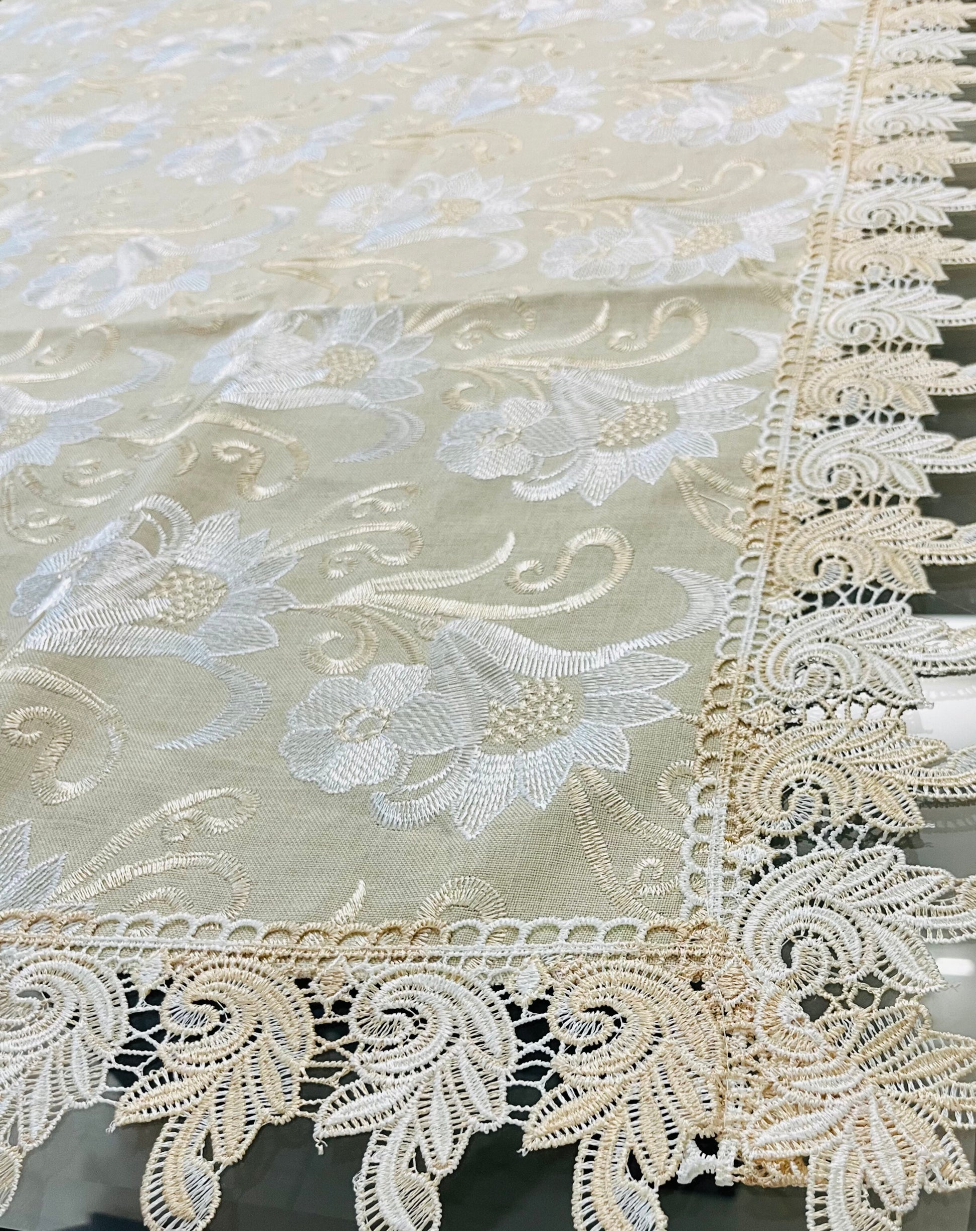Close-up of floral embroidery on an elegant lace dining tablecloth in gold and white with a scalloped border