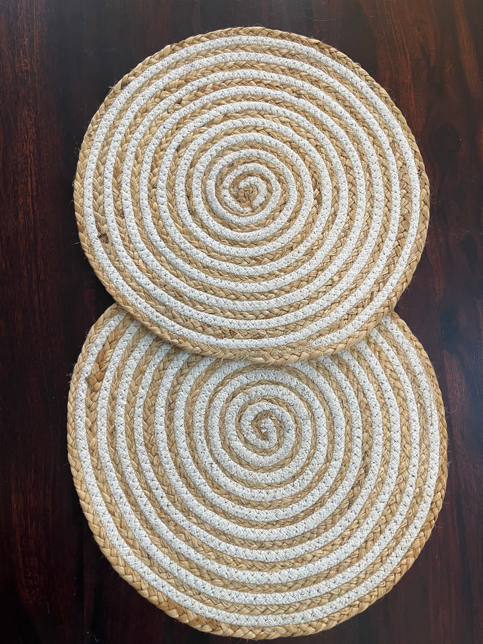 Set of 2 round braided jute placemats featuring a natural and white spiral design for rustic table décor