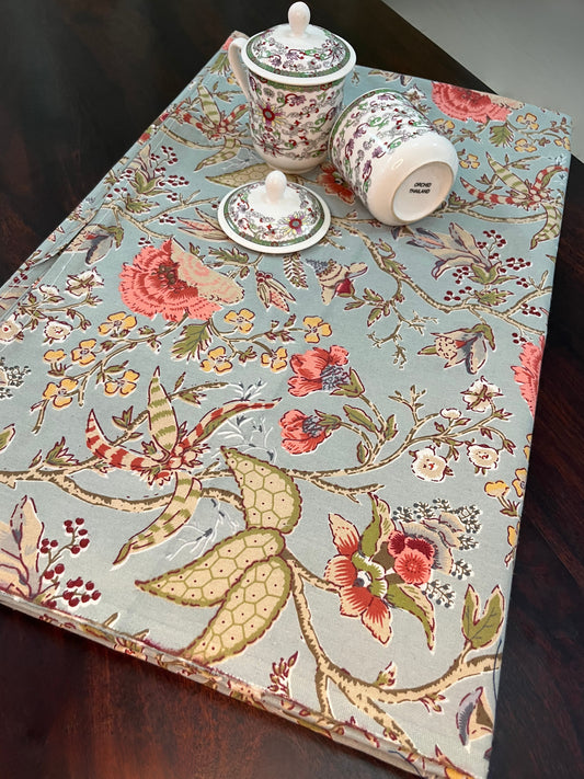 Beautifully styled dining table with a floral vintage botanical tablecloth in blue-green, featuring coral flowers