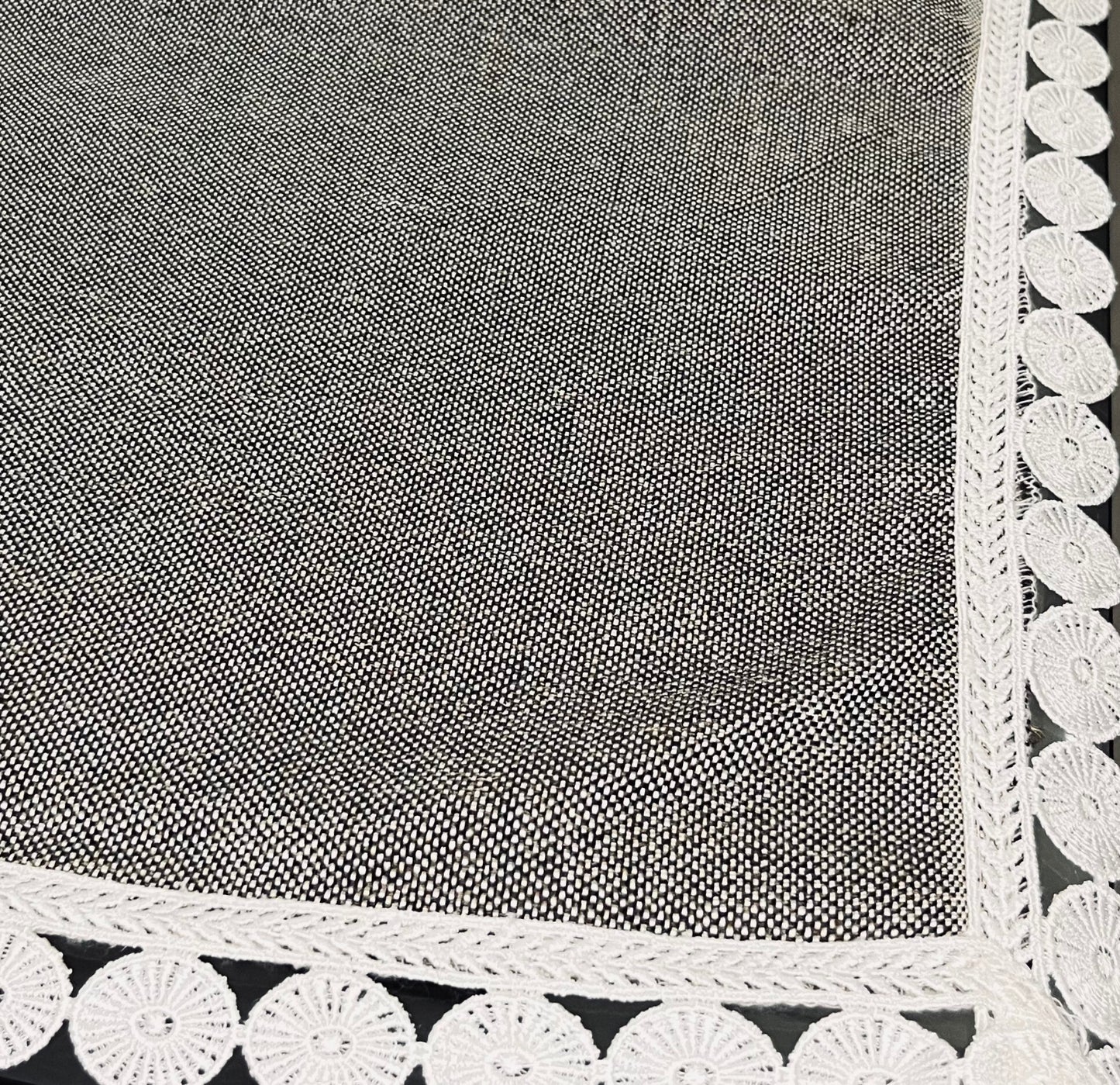 Close-up of dining table cover showcasing grey textured fabric with delicate lace trim and a scalloped white border