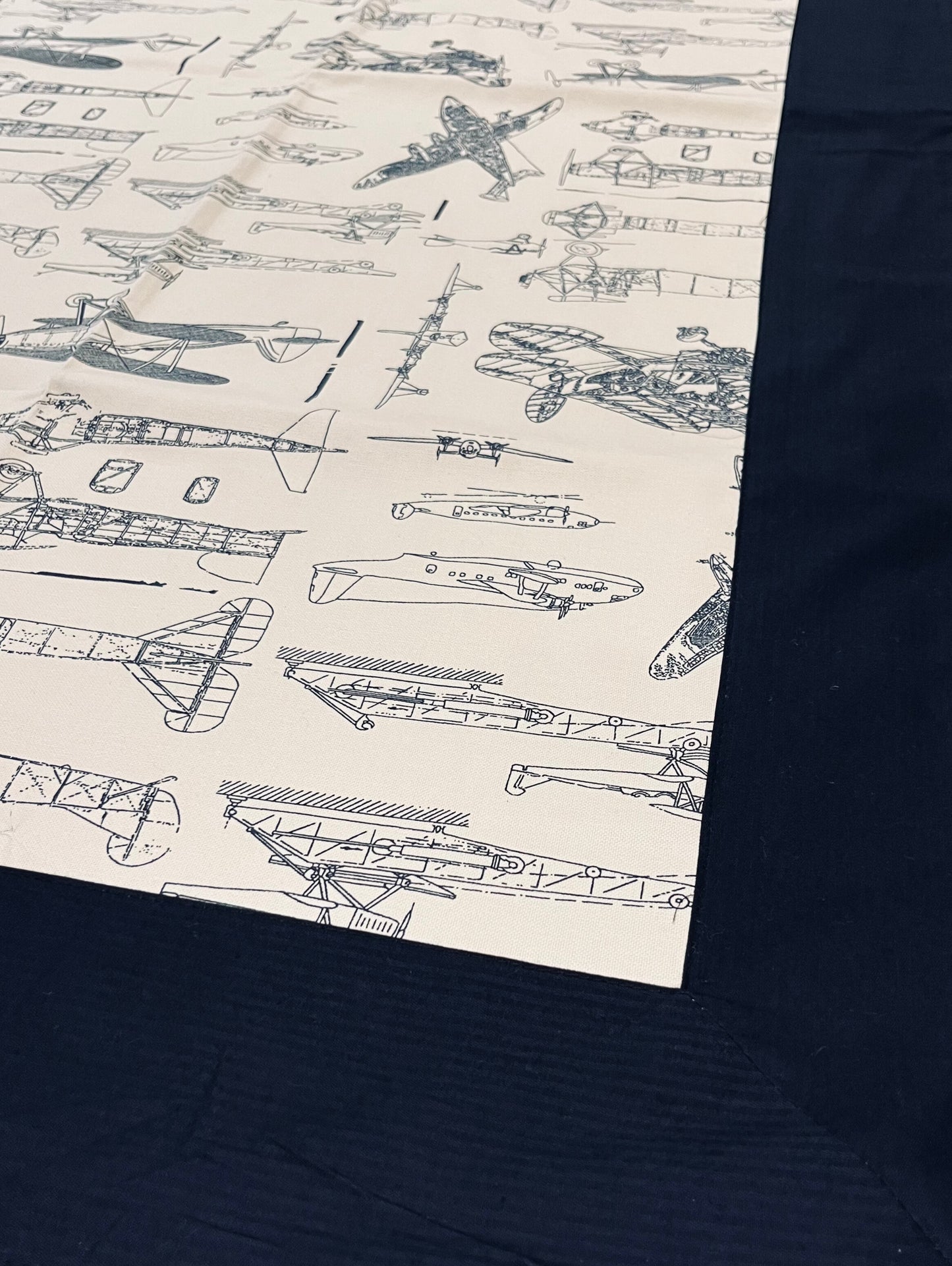 Close-up of vintage aircraft print dining table cover with an aviation-themed design on a cream background and navy blue border