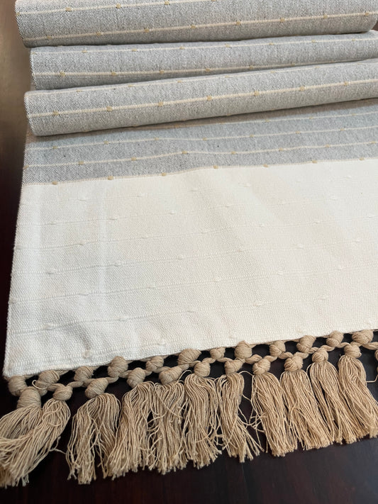 Close-up of decorative table runner showcasing intricate embroidery and tassel design in gray and white