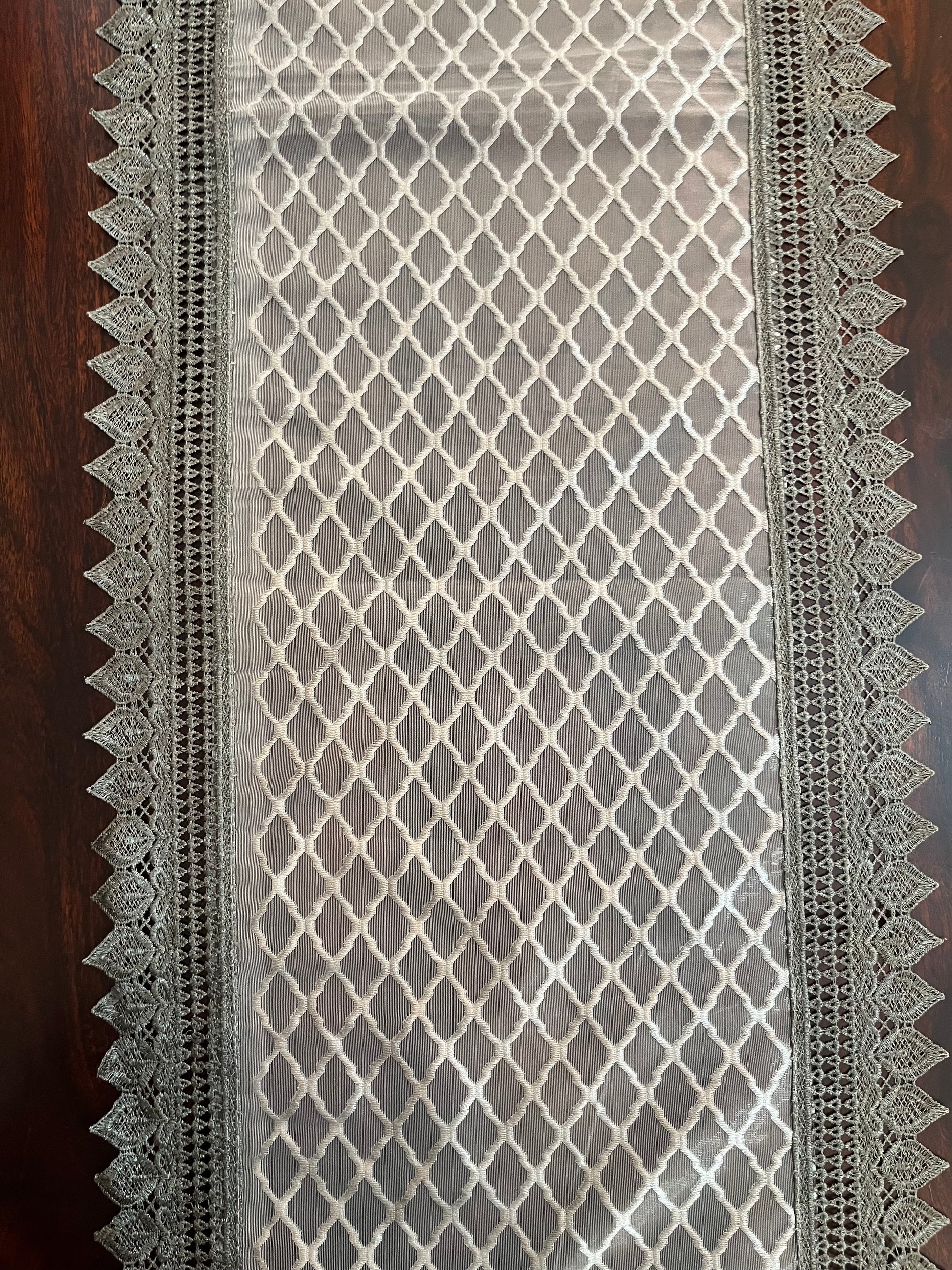 Close-up of elegant lace table runner showcasing a grey diamond pattern with a decorative crochet border
