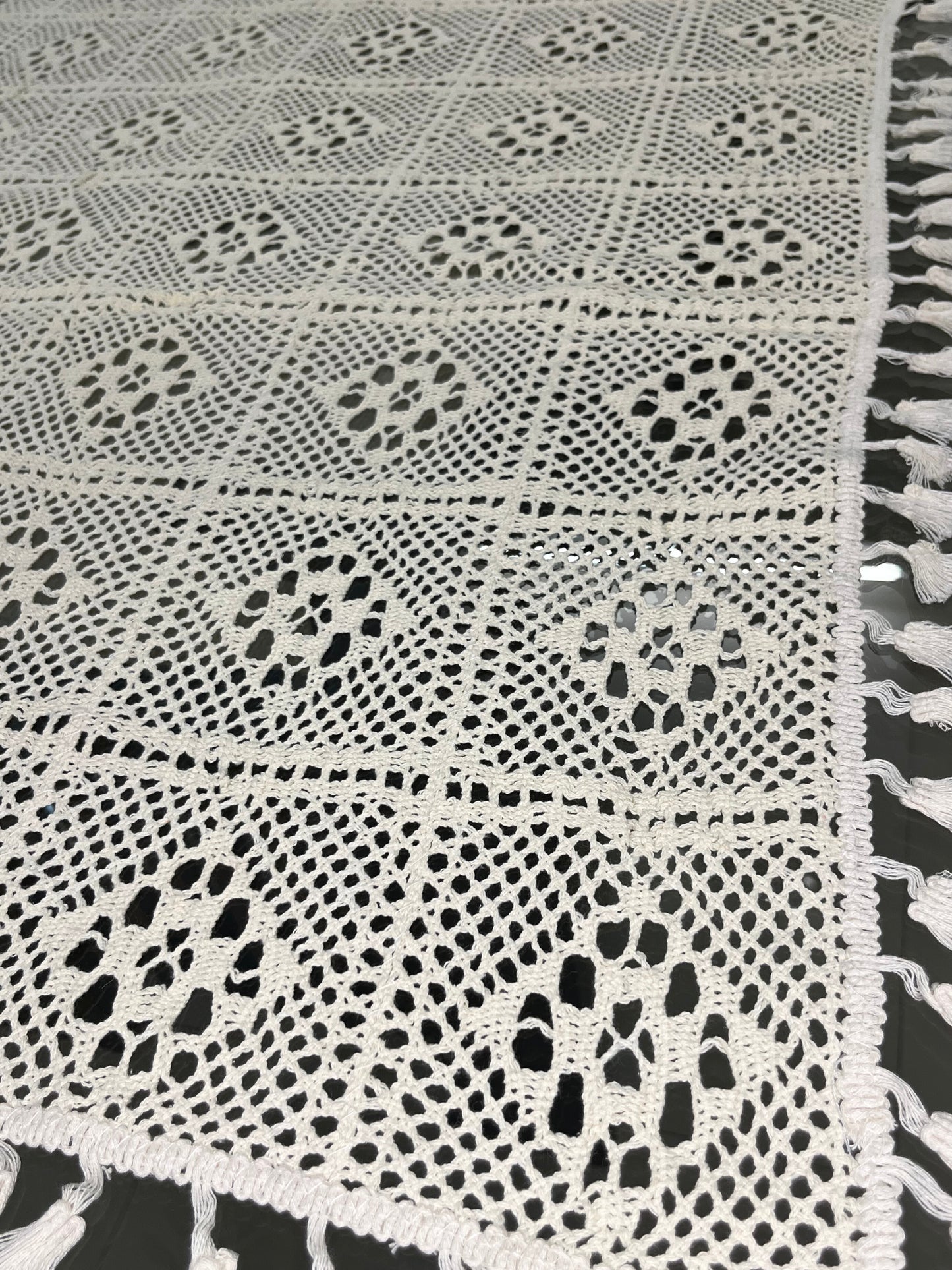 Close-up of crocheted dining tablecloth featuring a delicate diamond pattern and tassels in cream color