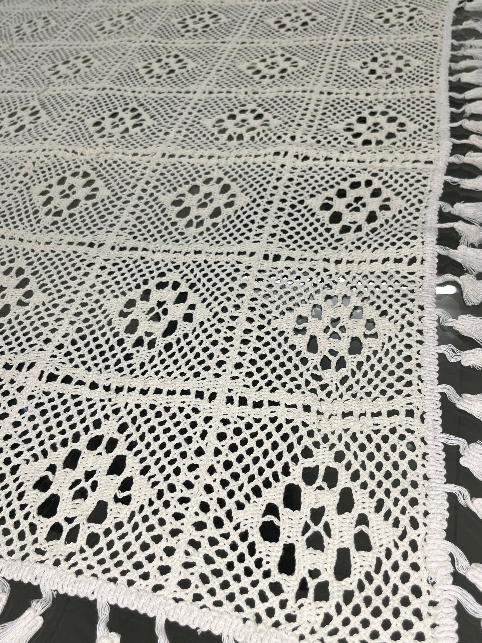 Close-up of crocheted dining tablecloth featuring a delicate diamond pattern and tassels in cream color