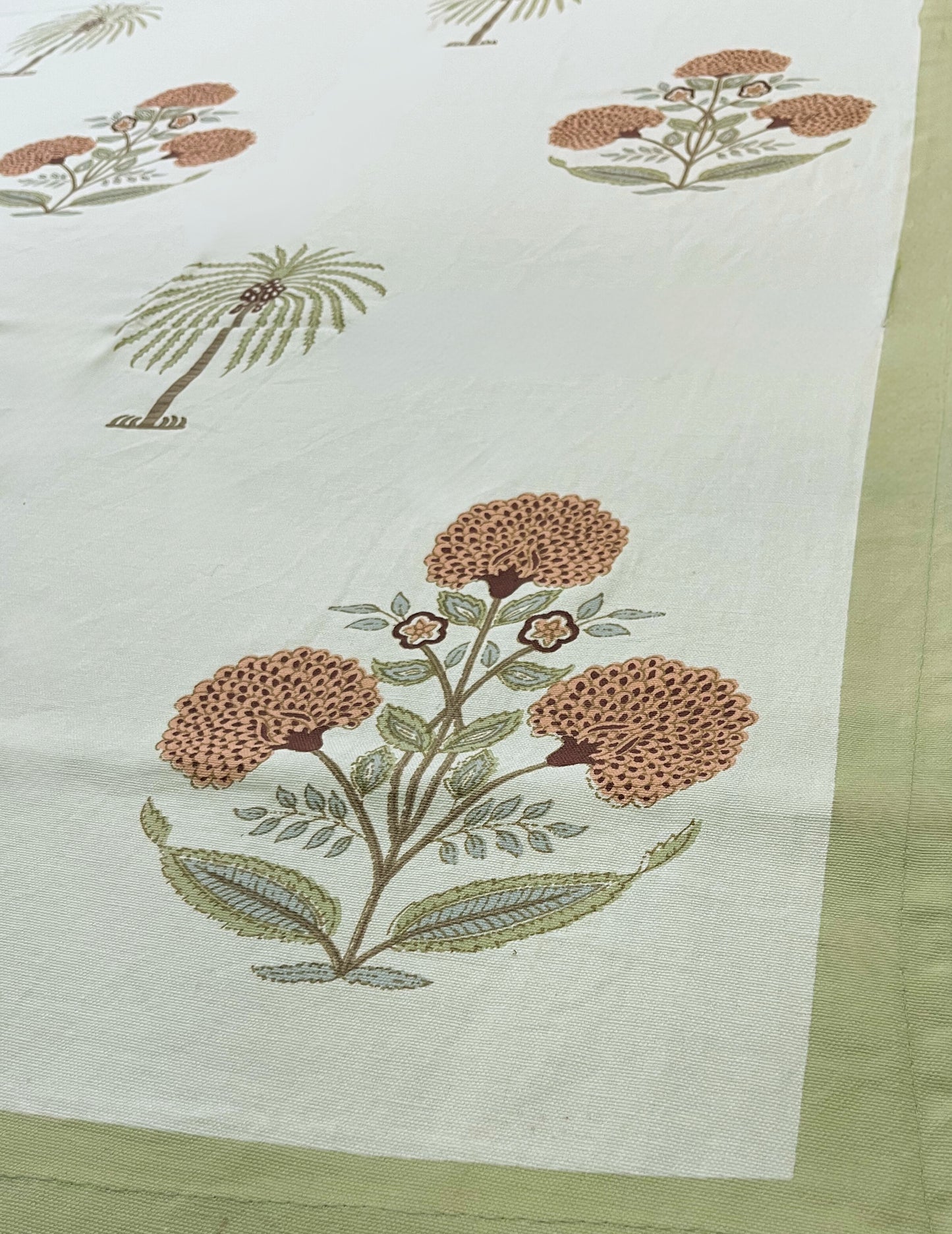 Close-up of tropical palm and floral print tablecloth featuring a green border on a white background