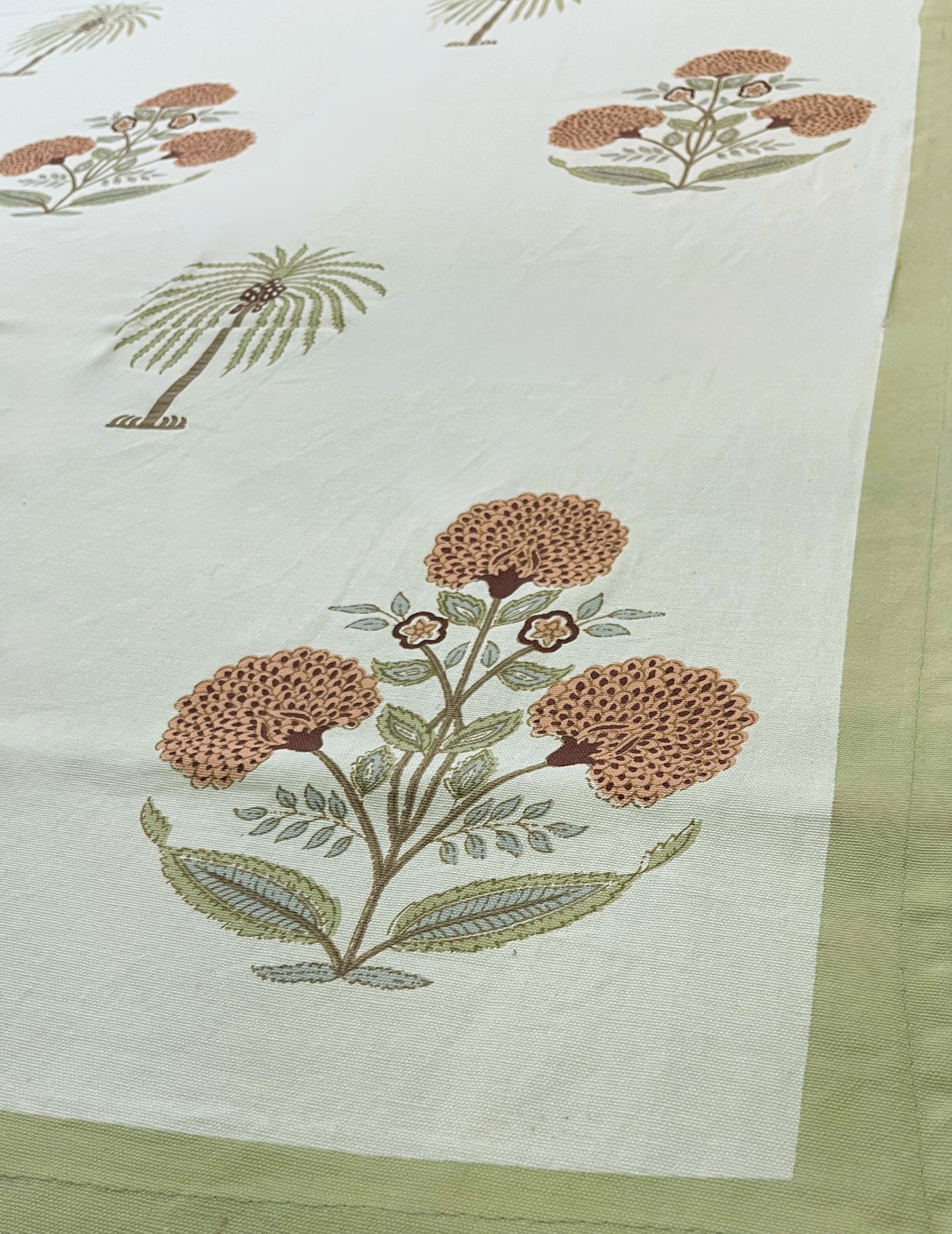 Close-up of tropical palm and floral print tablecloth featuring a green border on a white background